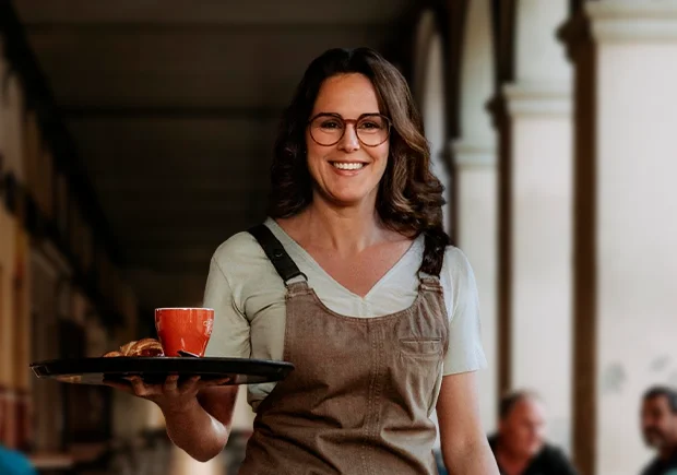 Cambrera duent una safata amb un cafè i un croissant a la terrassa d'una cafeteria.